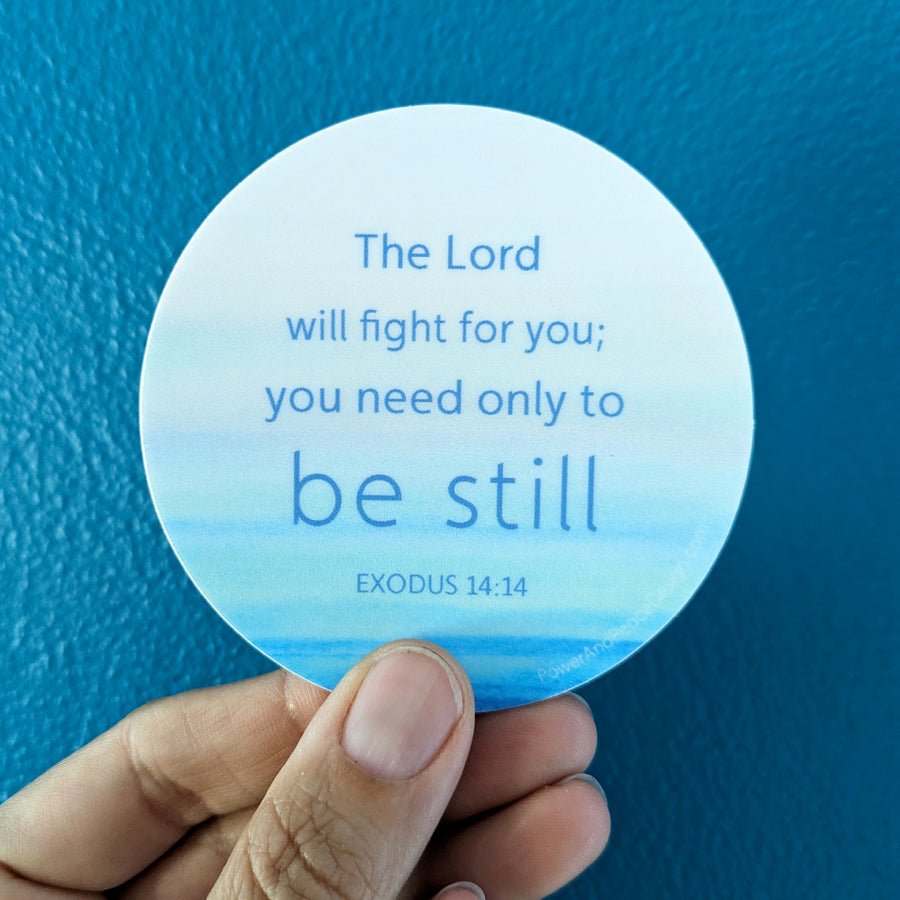 Encouraging Christian sticker with the Scripture from Exodus 14:14 The Lord will fight for you; you need only to be still. Seen held in a hand with a blue background.
