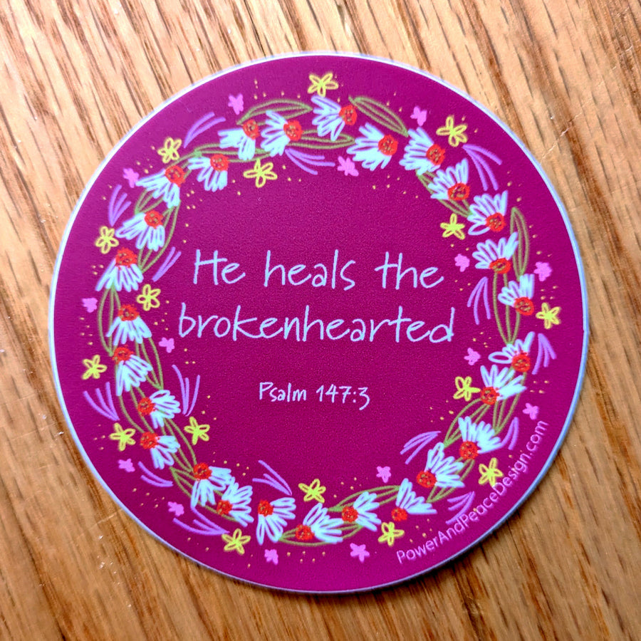 Bible verse sticker with Psalm 147:3 He heals the brokenhearted. Words are held within a floral wreath.