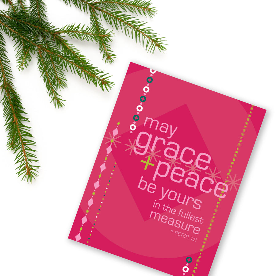 Berry red Christian Christmas card with geometric designs and text from 1 Peter 1:2 may grace and peace be yours in the fullest measure. Card is angled on white background. Evergreen brach in upper left corner.