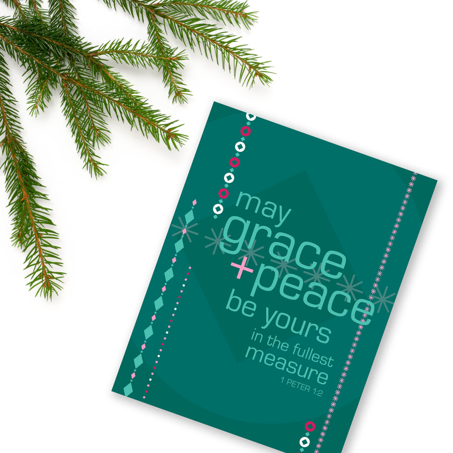 Evergreen, seafoam green, pastel pink, and berry Christmas card featuring the words of 1 Peter 1:2 May grace and peace be yours in the fullest measure. Card is angled on a white background with an evergreen branch in upper left corner.