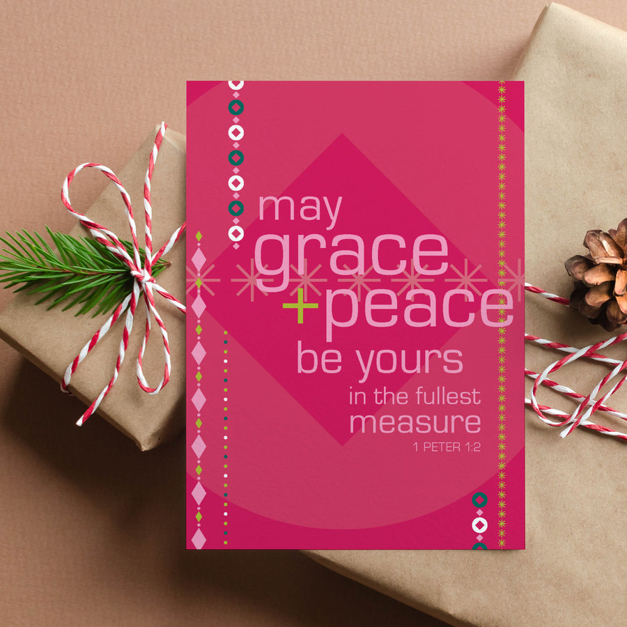 Red and pink Scripture Christmas card with 1 Peter 1:2 May grace and peace be yours in the fullest measure. Card is shown balanced on 3 gift packages wrapped in kraft paper with red and white twine.