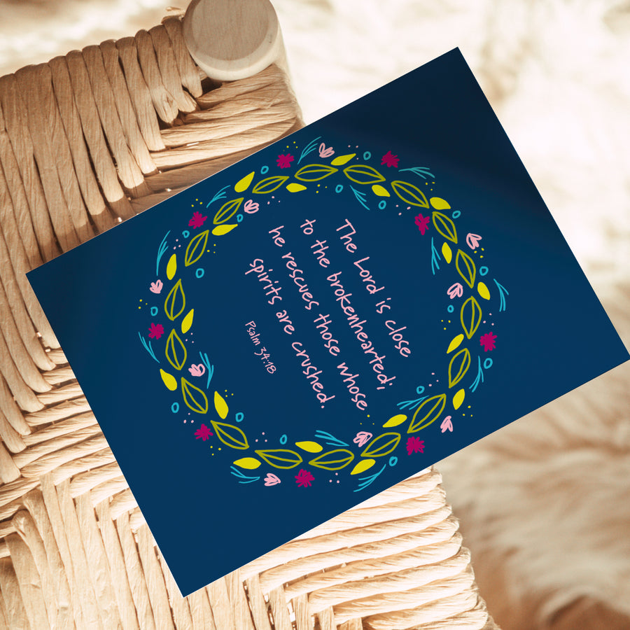Christian greeting card shown on chair. Text centered in floral wreath reads The Lord Is close to the brokenhearted; he rescues those whose spirits are crushed. Psalm 34:18.