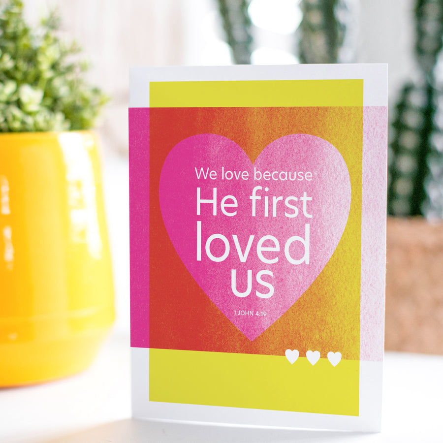 Wedding card with Scripture. Magenta and yellow card reads We love because He first loved us. 1 John 4:19.
