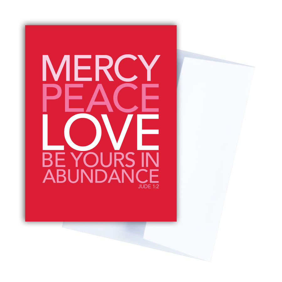Red Christian greeting card and white envelope. Text is in shades of pink and white and reads Mercy, peace, love be yours in abundance. Jude 1:2.