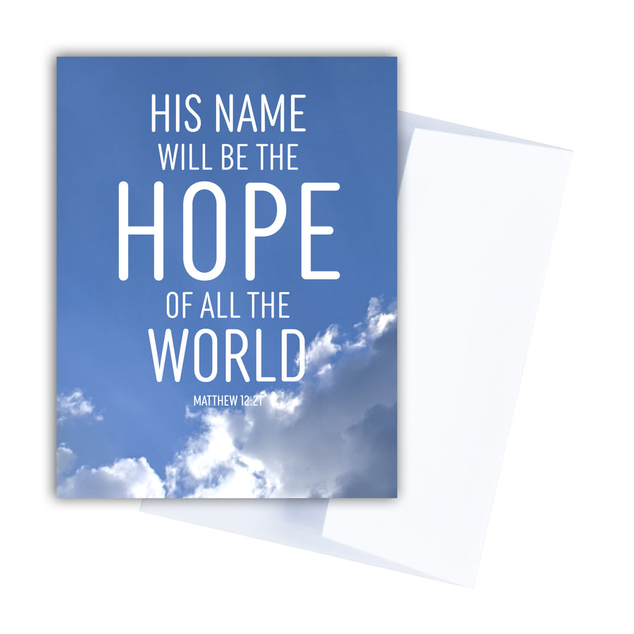 Blue Bible verse greeting card. Background is a blue sky with white clouds lit with sunlight. White text reads His name will be the hope of all the world. Matthew 12:21. Notecard shown with white envelope.