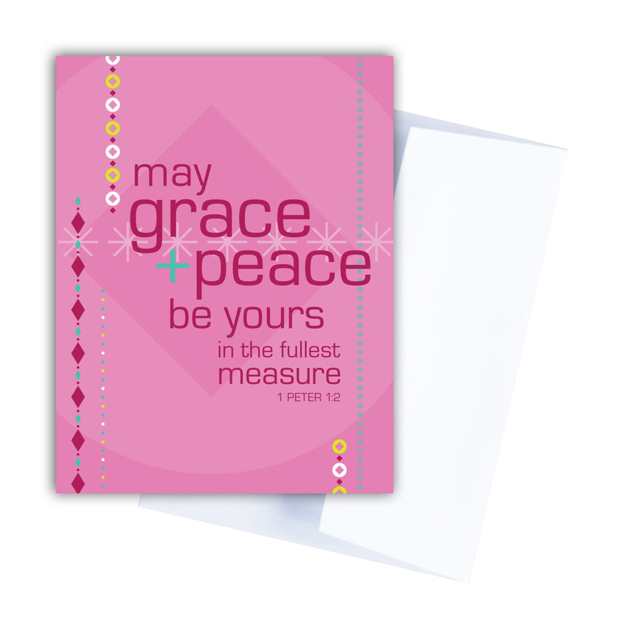 Pink Bible verse Christmas card with Scripture from 1 Peter 1:2 May grace and peace be yours in the fullest measure. Card features geometric illustrations of beaded garland and an ornament. Card overlaps white envelope.