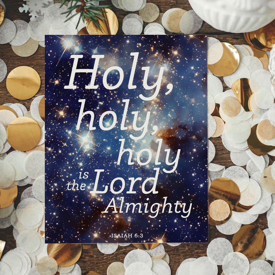Scripture Christmas card with an image of space. White lettering on top reads Holy, holy, holy is the Lord Almighty. Isaiah 6:3. Card shown on top of white and metallic gold confetti.