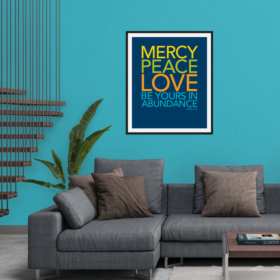 Living room scene with gray couch, teal walls, potted plant, and framed art print on wall. Art is navy blue with text reading Mercy, peace, love be yours in abundance. Jude 1:2. Text in yellow, lime green, orange, and teal. 