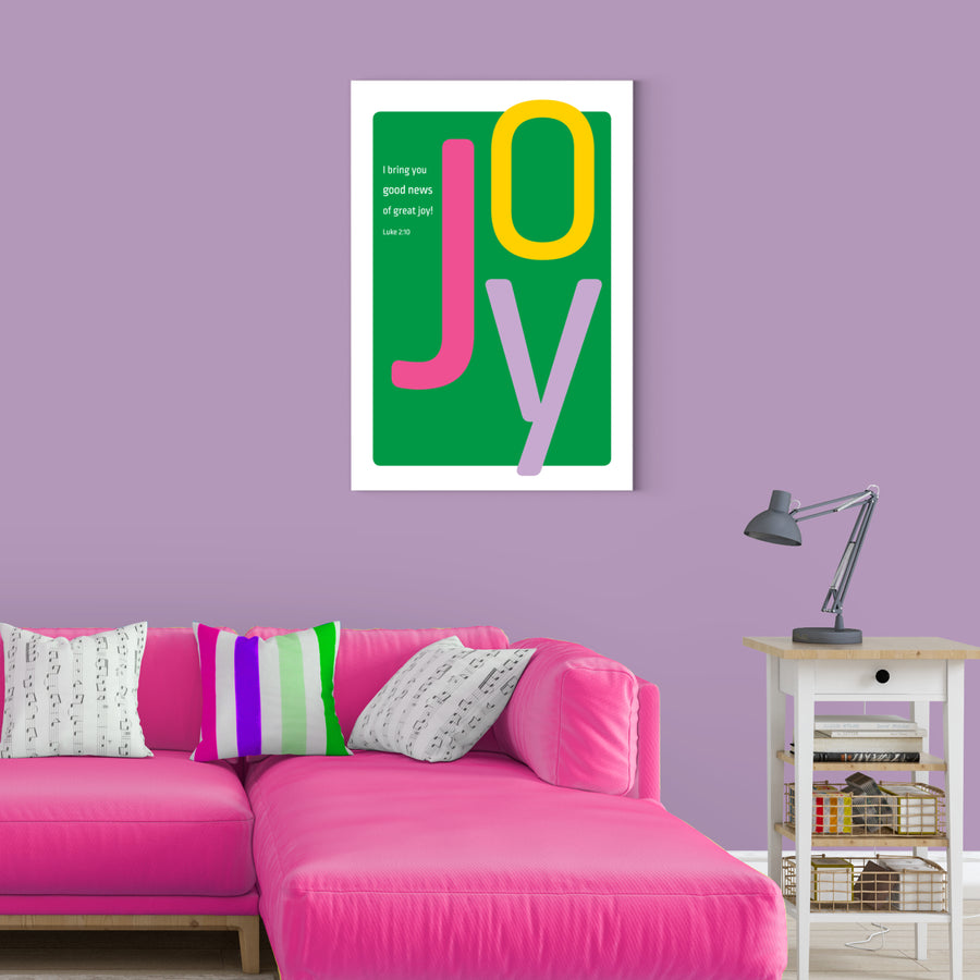 Colorful living room with lavender walls and pink couch. Framed kelly green Bible verse art hangs on wall. Christian art featuring large letters spelling JOY. Smaller white text reads I bring you good news of great joy! Luke 2:10. Art in front has a kelly green background. J is magenta. O is yellow. Y is lavender.