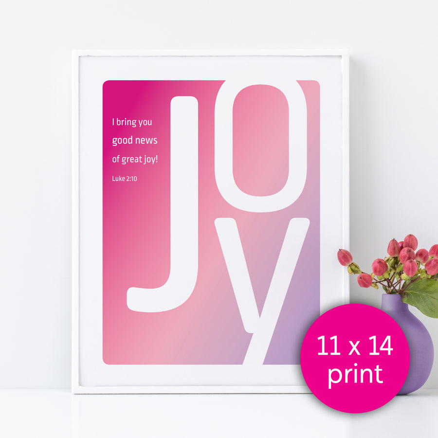 Framed Christian typography artwork featuring large letters spelling JOY. Background of art is magenta, pastel pink, and lavender ombre. Smaller white text reads I bring you good news of great joy! Luke 2:10. Large white letters spell JOY. Pink circle in bottom right labels the image 11x14 print.