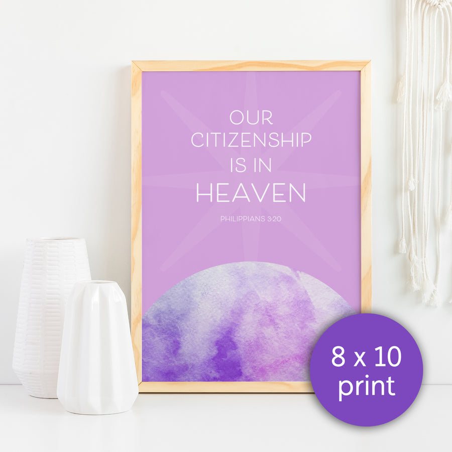 Lavender artwork in a light wood frame against a white background. Christian art reads Our citizenship is in heaven. Philippians 3:20. Words are centered in upper half of art with a subtle lighter lavender star behind them. Words rise above a cropped purple, pink, and lavender watercolor planet. Purple circle in lower right labels art as 8x10 print. Two white vases are in left foreground. Part of a white macrame weaving hangs in upper right corner.