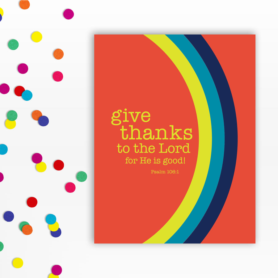 Front of an orange Bible verse greeting card with the words: give thanks to the Lord for He is good! Psalm 106:1. A curved rainbow stretches from top to bottom in navy blue, teal, and acid yellow. Confetti to the left of the card.