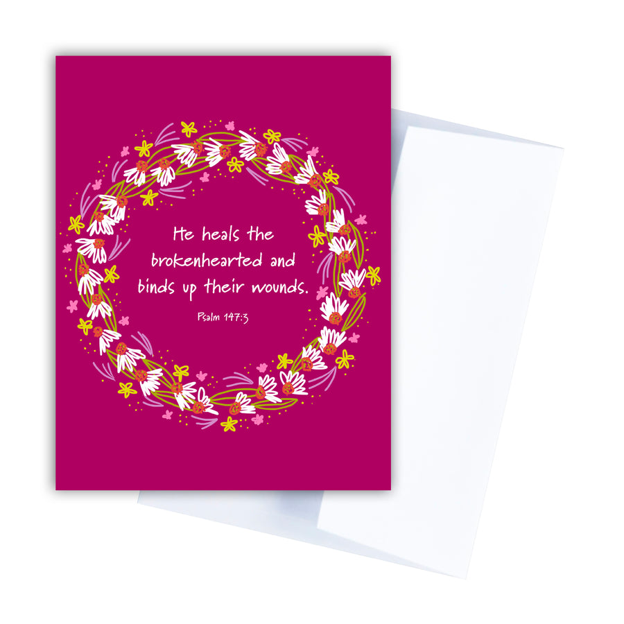 Berry pink Christian sympathy card with Psalm 147:3 He heals the brokenhearted and binds up their wounds. Scripture is circled by a wreath of wildflowers and daisies.