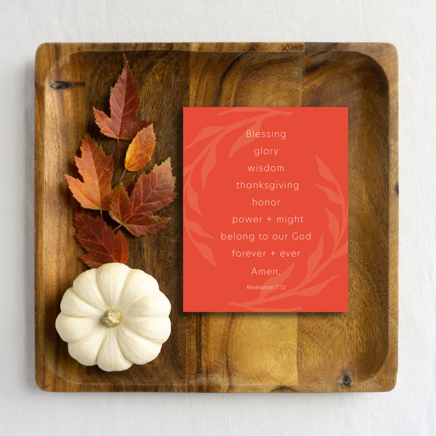 Orange Thanksgiving card reading Blessing, glory, wisdom, thanksgiving, honor, power and might belong to our God forever and ever. Amen. Revelation 7:12. Bible verse greeting card is laying on wood tray with autumn leaves and white pumpkin. 