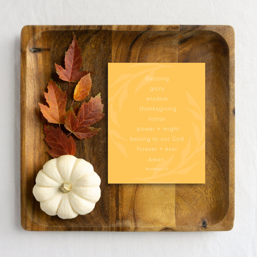Buttercream yellow Thanksgiving card reading Blessing, glory, wisdom, thanksgiving, honor, power and might belong to our God forever and ever. Amen. Revelation 7:12. Scripture greeting card is laying on wood tray with autumn leaves and white pumpkin. 