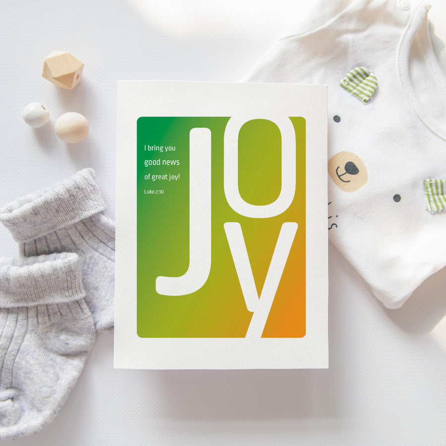 Christian pregnancy announcement or new baby card with Luke 2:10. I bring you good news of great joy! Luke 2:10. Card shown near baby socks and a onesie.